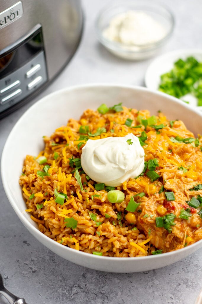 This slow cooker fiesta chicken and rice recipe is a simple weeknight dinner that the whole family will love. You can use this recipe for taco night or burrito night, for an easy meal prep recipe, or for homemade nachos at a family gathering or football party. It's full of flavor, perfectly cheesy, and gets in some vegetables with green peppers and onions. With under 30 minutes of hands-on time and only one dish, you will love this set it and forget it meal! #slowcookerfiestachicken #slowcookerchicken #footballrecipes #burritofilling #crockpotchicken