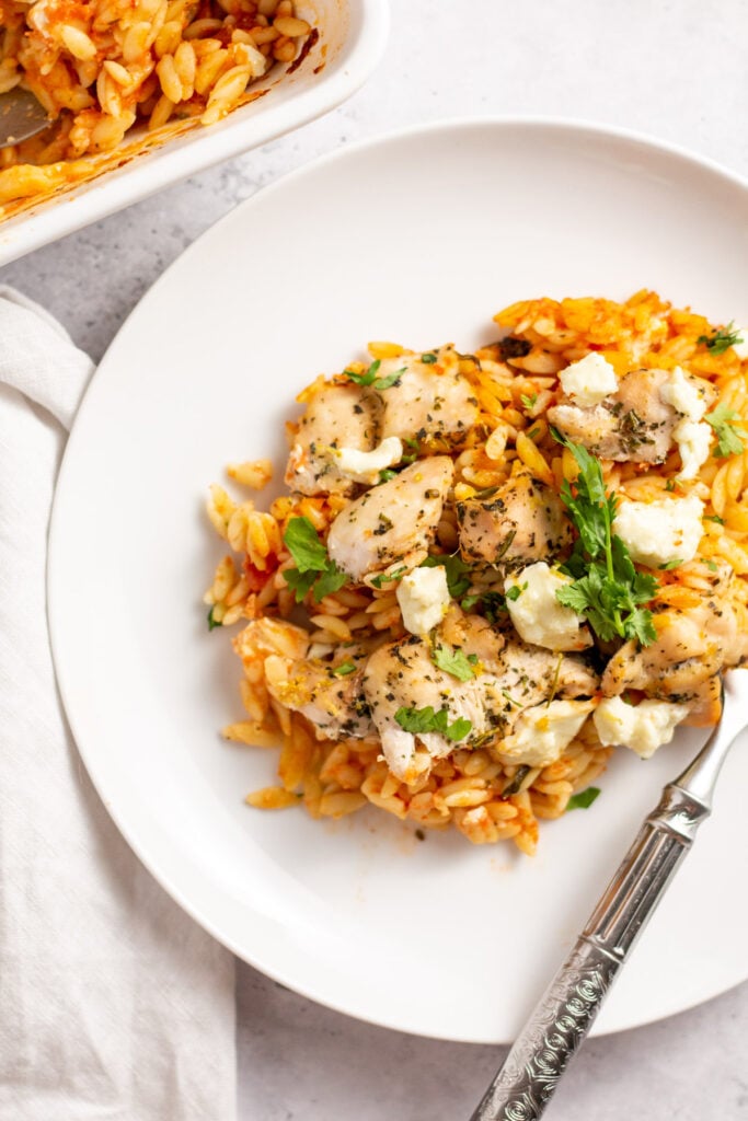 This Greek chicken orzo bake is a really easy and delicious pasta casserole recipe that is made with seasoned chicken, tomatoes, spinach, lemon and plenty of feta! It's simple to make gluten-free, uses few ingredients, and reheats well so you can use this not only as a weeknight dinner, but as a meal prep recipe as well. #pastabake #chickencasserole #chickenpastabake #greekchicken #orzochicken