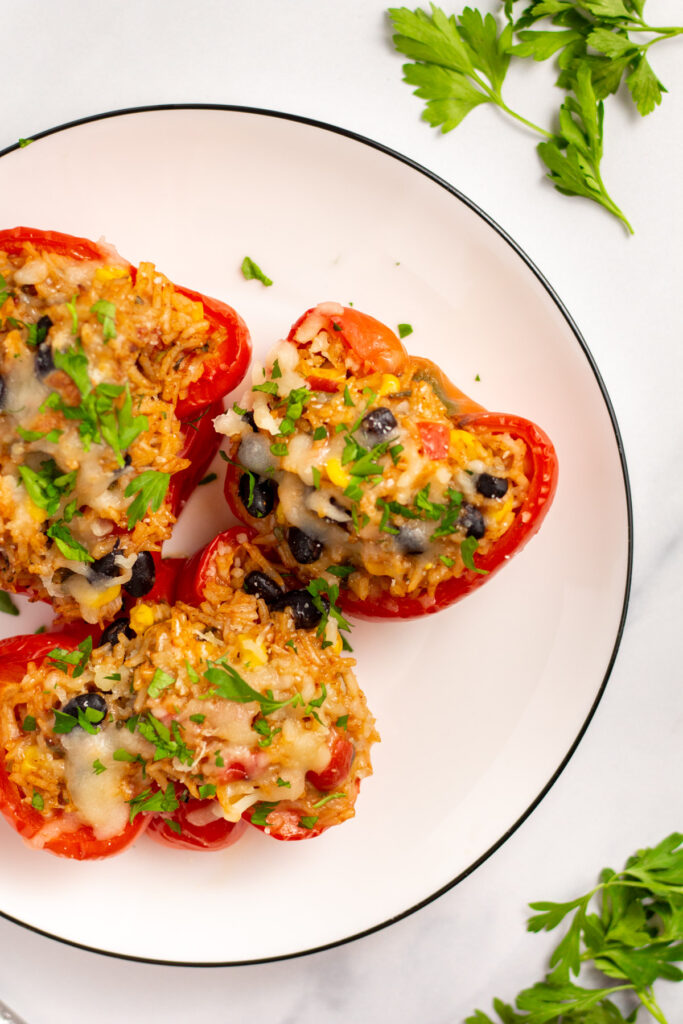 These vegetarian stuffed peppers are full of healthy vegetables like tomatoes, cilantro, corn, green chiles and onions, packed with rice, black beans and all mixed together with a delicious taco seasoning. They're easy to make for a weeknight meal, and to store and reheat for meal prep! They're gluten-free, vegan and vegetarian, and can be made dairy-free! It's a budget friendly recipe the whole family will love. #meatlessrecipes #veganrecipes #stuffedpeppers #dairyfree #vegetariandinner #glutenfreedinner #mealprep